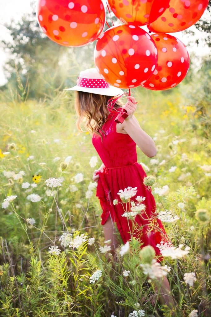 Femme habillée en rouge dans un champ avec des ballons rouges